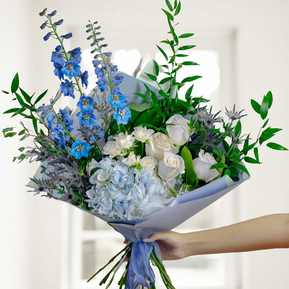 Bouquet of blue and white flower bouquet  held by a hand against a neutral background