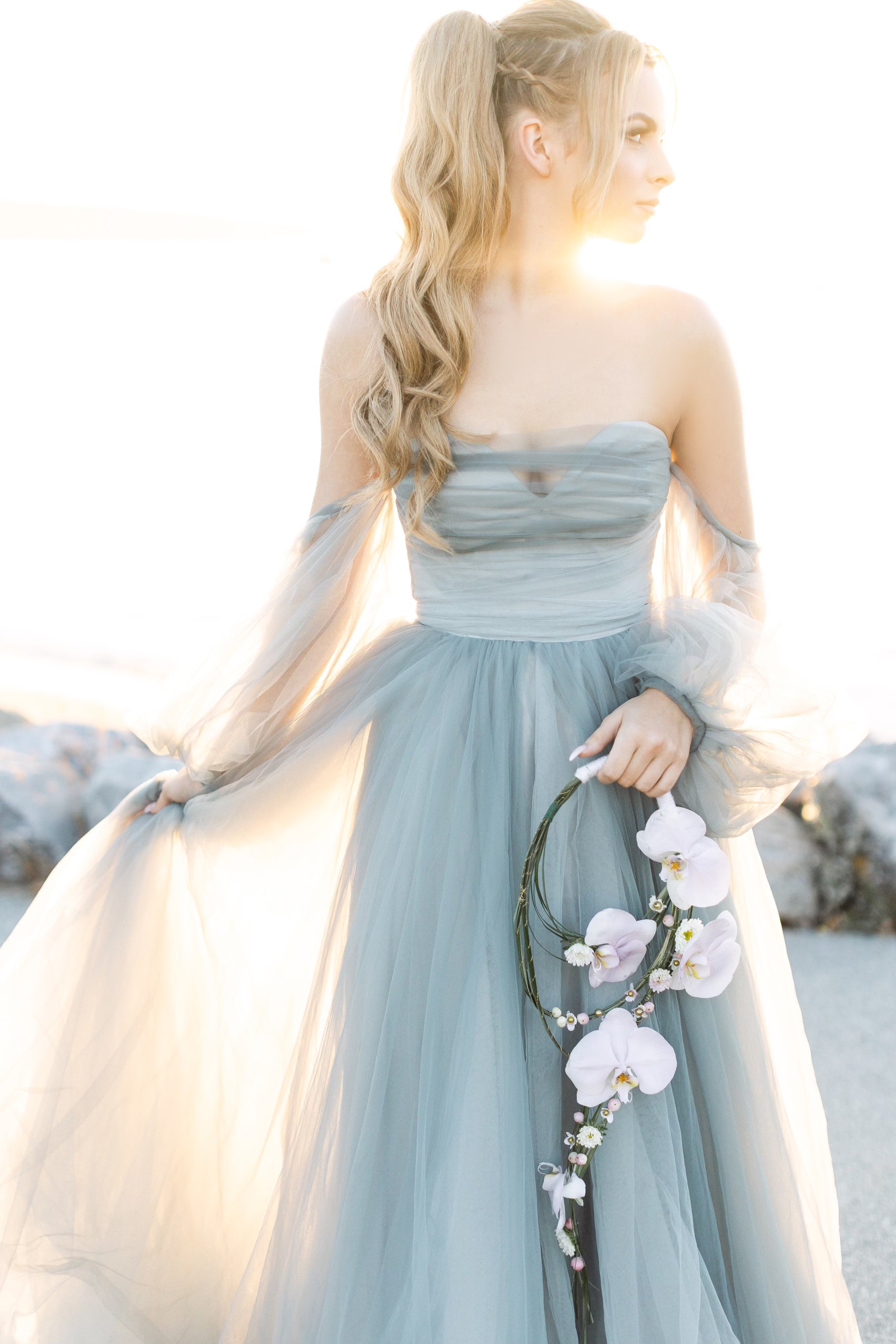 Woman in a light blue dress holding flowers against a blurred natural background