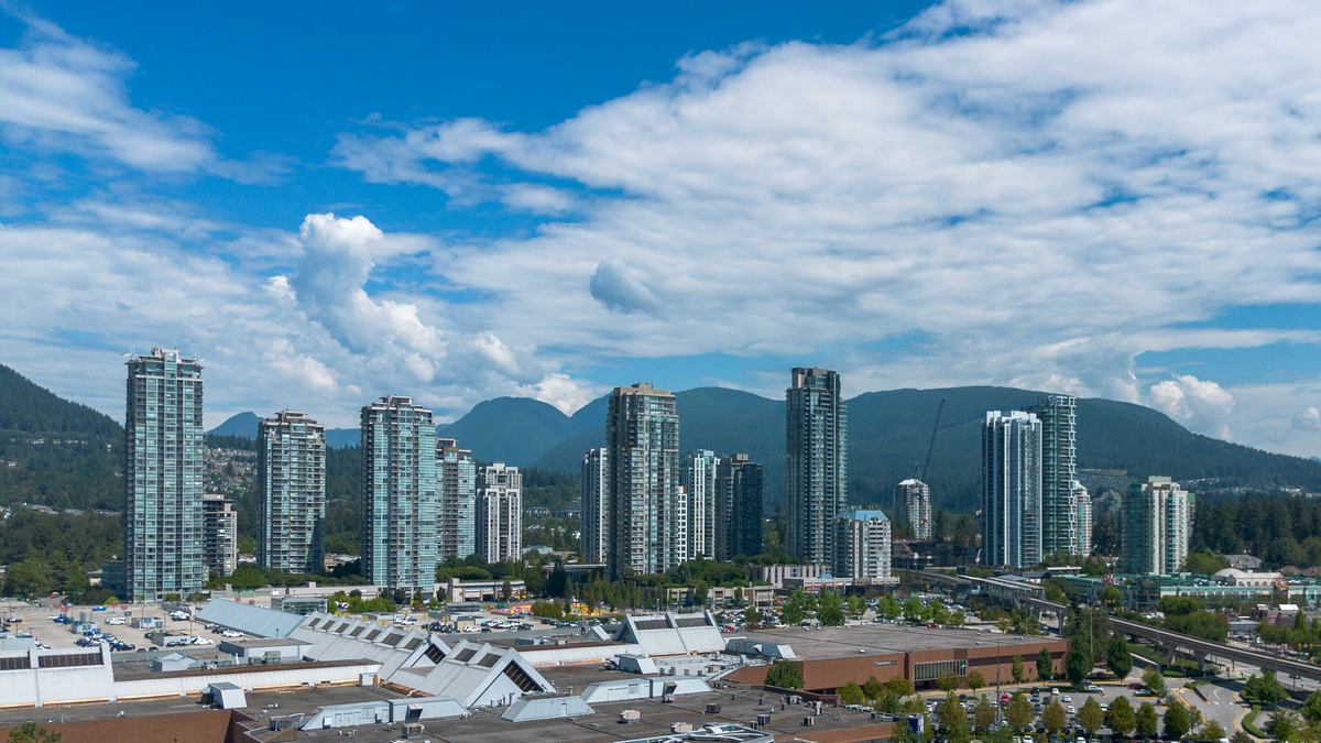City skyline with tall buildings and mountains in the background under a blue sky with clouds.