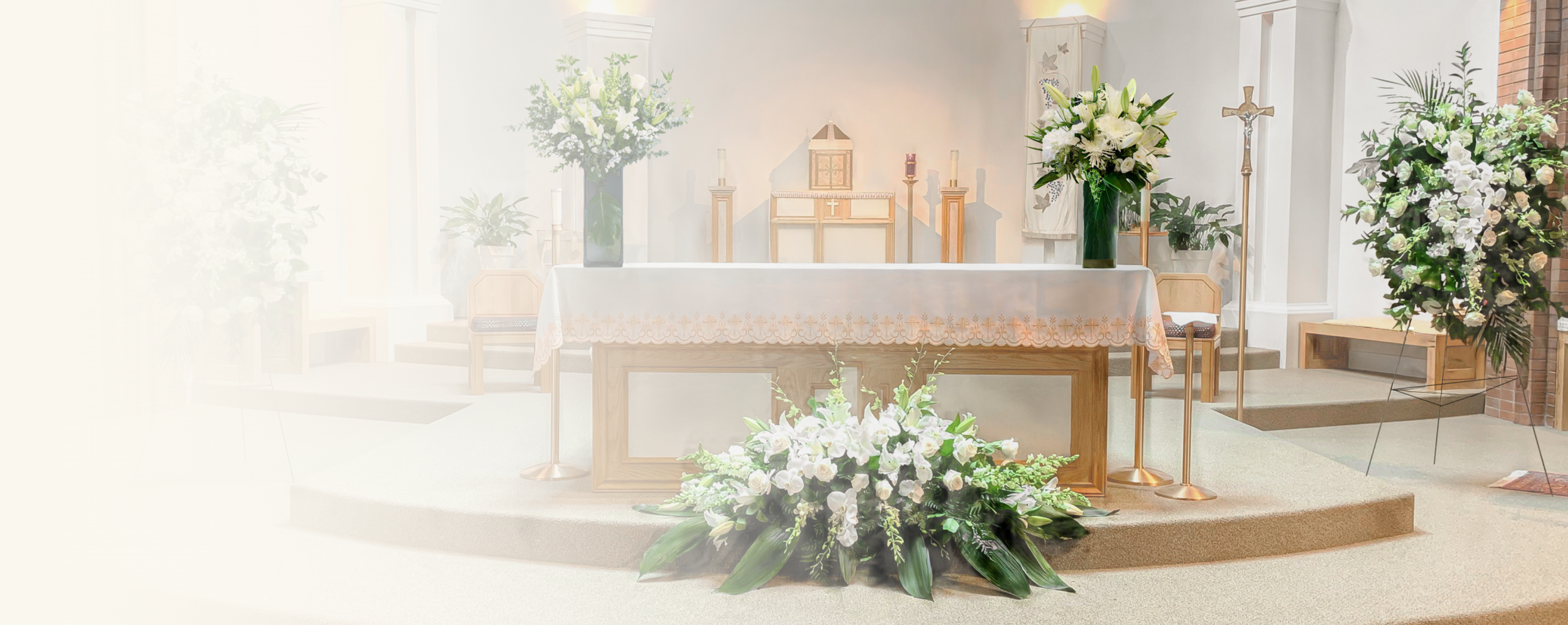 A softly lit church interior with a raised altar, white floral arrangements, candles, and a cross on a stand. The scene is bright and hazy, creating a dreamy, reverent atmosphere.