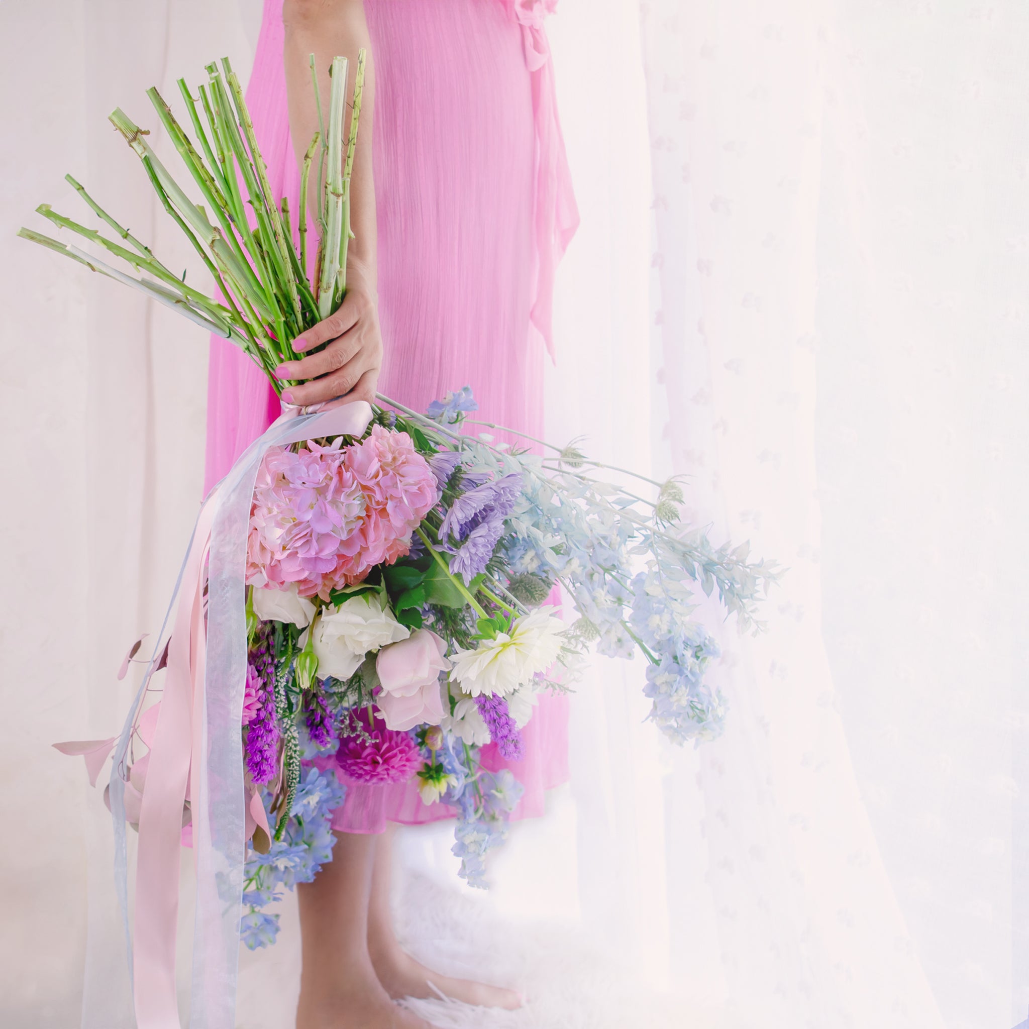A person holding a beautiful premium flower bouquet with a mix of colors, predominantly pink and blue, with available seasonal flowers.