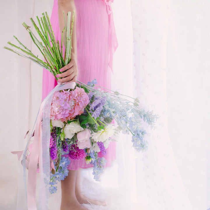 A person holding a beautiful premium flower bouquet with a mix of colors, predominantly pink and blue, with available seasonal flowers.