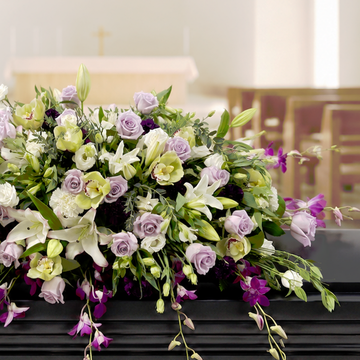 A large floral casket arrangement with white, purple, and pale green flowers draped over a black casket in a church setting.